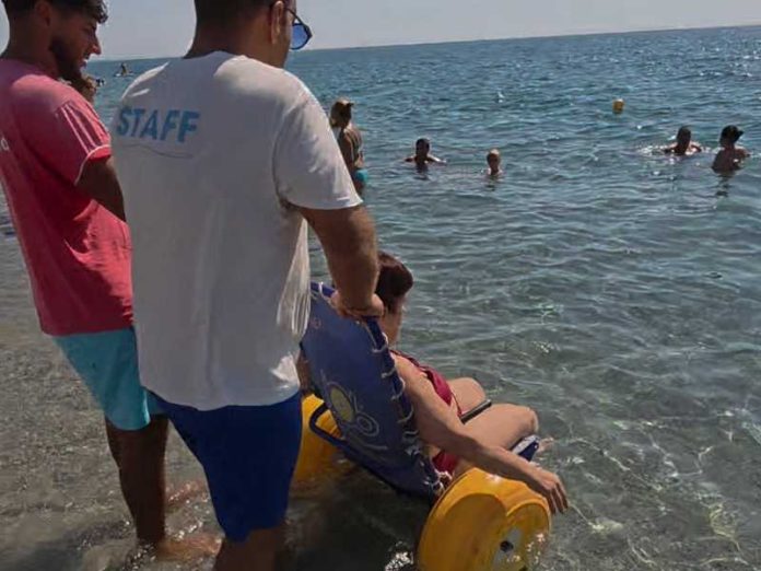 Due bagnini accompagnano una persona con disabilità in acqua.